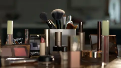 Makeup products, including mascara, eyeshadow, lipgloss and brushes, spread out on a table