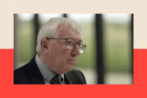 Panorama Dr Mike Hall wears glasses and a suit, and looks away from the camera