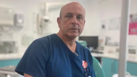 Keith Garber sitting in his dentist practice with blue dentist scrubs.