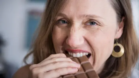 Getty Images A woman takes a bite from a big bar of chocolate