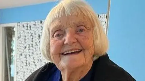 Nias family handout Jenny Nias, smiling, with white coloured bob hair, wearing a black coat.