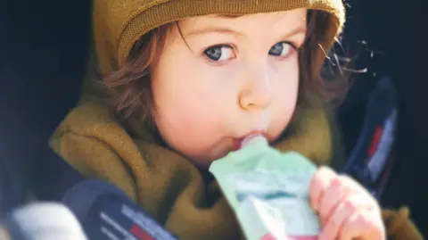 Getty Images A stock image of a young child with brown hair sucking on a pouch of food
