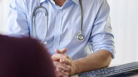 Getty Images Man in light blue shirt wears stethoscope round his neck and clasps his hands 