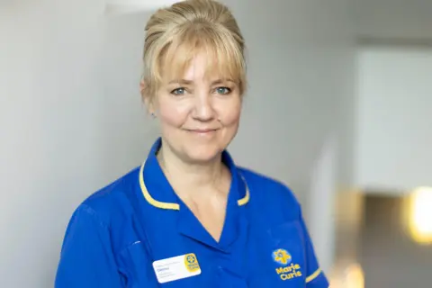 Marie Curie Diana, a middle-aged blonde woman, smiling in her blue Marie-Curie nurses uniform