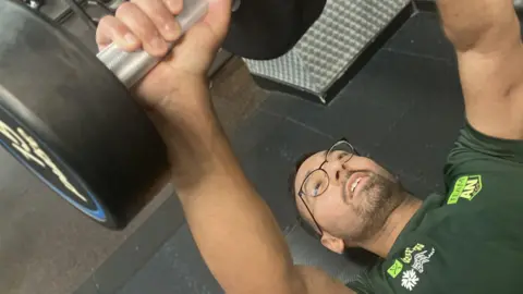 Raj a 32 year old mature student at the University of Liverpool is working out in the gym. He focusses on fitness after having a successful stem cell transplant five years ago to treat his blood cancer. He is lying on the floor lifting some heavy weights 