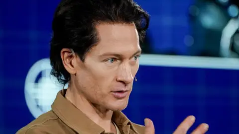 Bloomberg via Getty Images Bryan Johnson stands on a stage to give a speech, wearing a small microphone