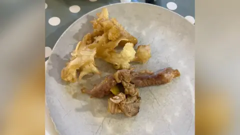 Supplied A plate of food. It appears to be a curled up piece of meat and a few bits of cauliflower.