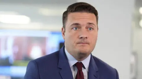 PA Media Wes Streeting has short brown hair and is wearing a blue suit jacket with red tie.