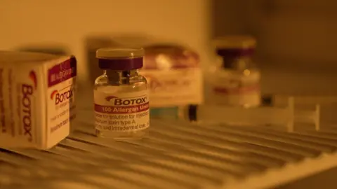 A close-up of a vial labelled “Botox” on a refrigerator shelf, with other vials and packaging visible in the background.
