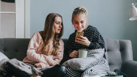 Getty Images Two female teenage friends using social media, sitting on a sofa