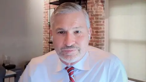 The Macrons' lawyer Tom Clare, a white man with grey hair, stubble and wearing a white shirt and red tie 