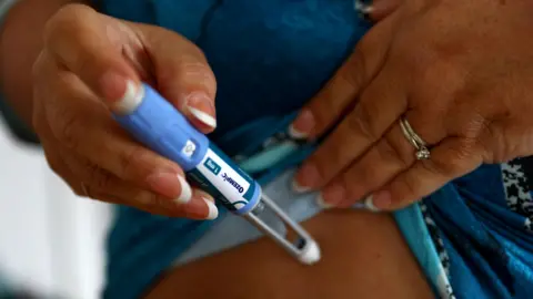Reuters A close up of a woman's hands - she is holding an injection pen and is about to inject a weight  loss drug into her abdomen. 