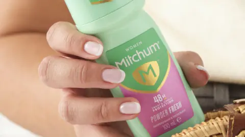 Mitchum A hand holding a green and pink bottle of Mitchum powder-fresh roll-on deodorant.
