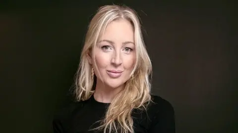 Dr Liz Murray Liz is wearing a black top and is stood against a black background. She has long blonde hair and is wearing gold-coloured earings.