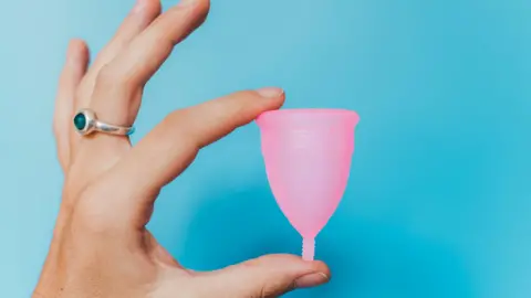 Getty Images Woman holding a pink menstrual cup on blue background 