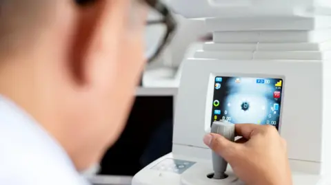 Getty Images  Rear view of an ophthalmologist using a modern eye test equipment tool to perform a vision exam with his patient at an ophthalmologist's clinic.