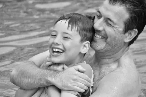 Hutchinson family Black and white image of Jack Hutchinson and dad Mark, playing in water and smiling.
