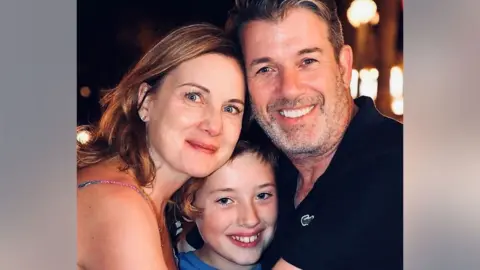 Hutchinson family Arlene Hutchinson and her son Jack and her late husband Mark all with their heads together and smiling at the camera.