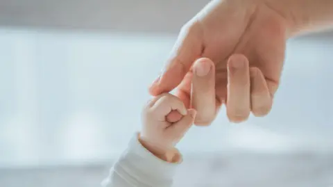Getty Images A small baby's hand holding the finger of a larger hand
