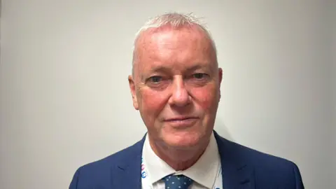 A man in a blue suit is looking at the camera. 