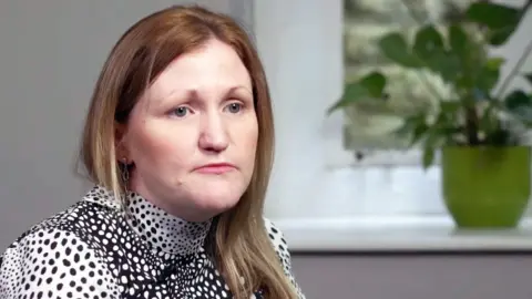 Active Patients A photo of Karen Booth, looking serious and deep in thought. Her blondish-brown hair is loose and she is wearing a spotted black and white top. A pot plant is in the background on a white windowsill. 