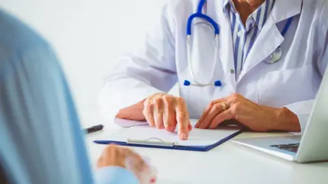 Getty Images An anonymous person in a white coat with a stethoscope is pointing at a clipboard