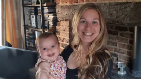 Victoria Roberton A woman with long blonde hair holding a baby smiling. 