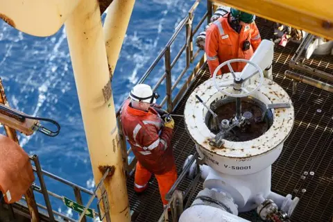 Getty Images Two workers wearing orange overalls and a hard hats fix a pig launcher on the Armada gas condensate platform, operated by BG Group Plc, in the North Sea, off the coast of Aberdeen.